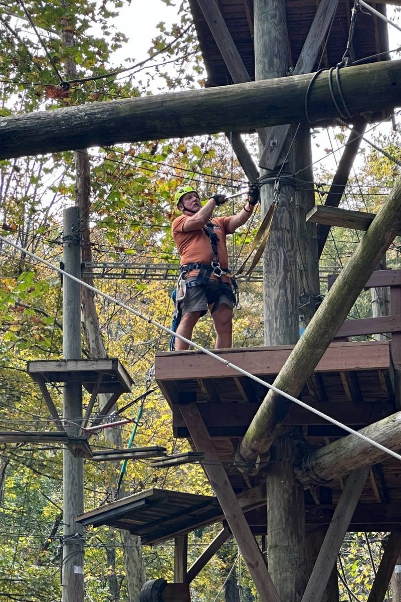 ARCL Innovations worker examining ropes course construction, wooden platforms and cable connections on an elevated challenge course.